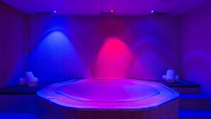 A spa room with a hot tub, tiled walls, and two towels on side tables.