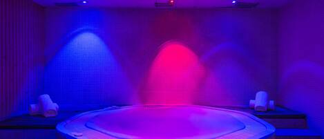 Une salle de spa avec un jacuzzi, des murs carrelés et deux serviettes posées sur des petites tables d’appoint.