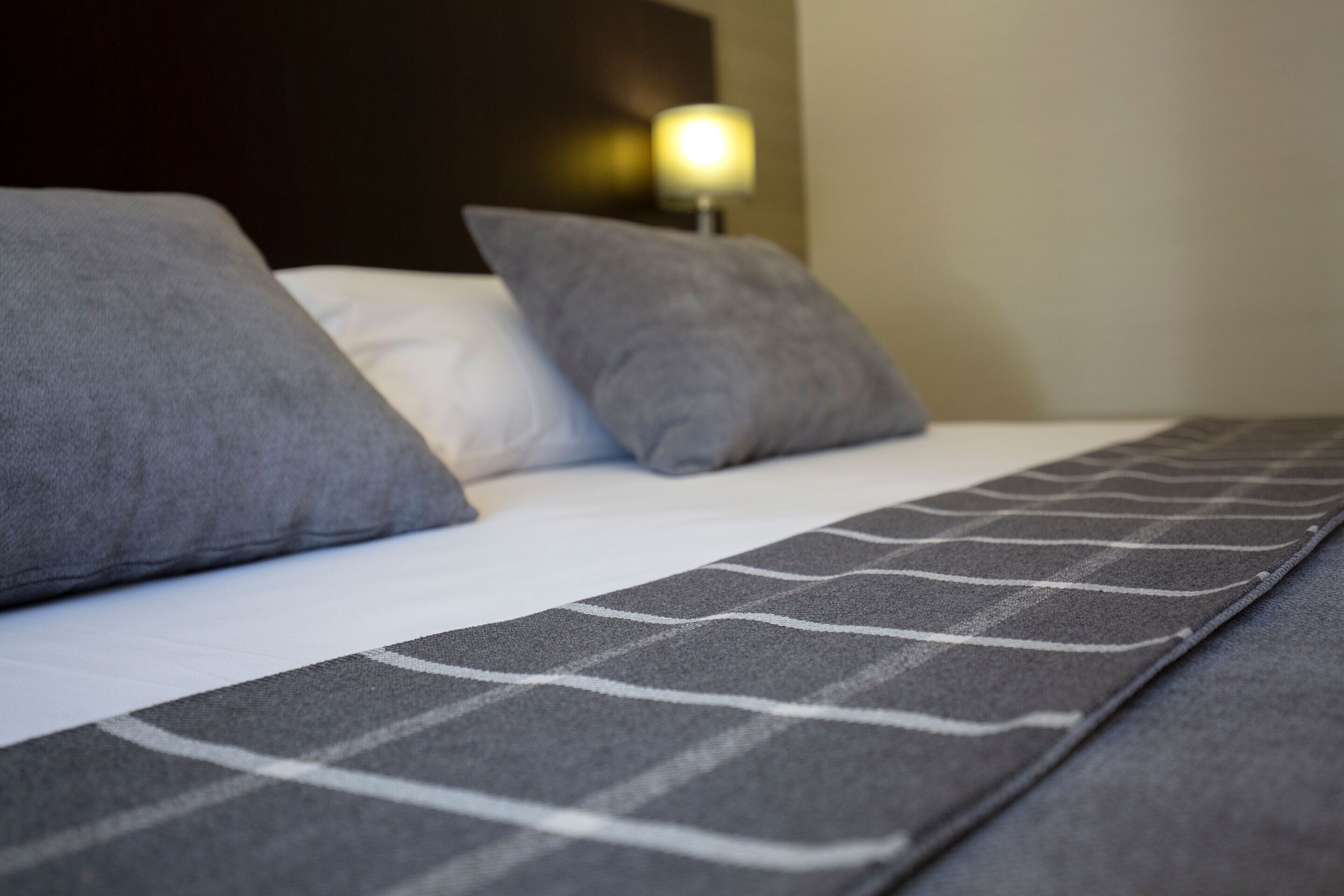 A bed with grey and white bedding, a headboard, and a bedside lamp.