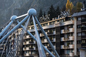 A modern hotel with a prominent sign, multiple balconies, and a view of mountains in the background. - Hotel Màgic Andorra la Vella by Nexta (Andorra la Vella)