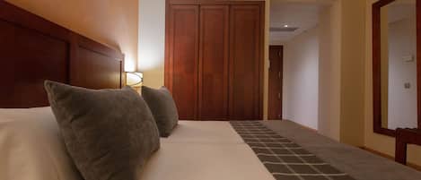 A hotel room with a bed, two pillows, a nightstand, a lamp, and a wardrobe.