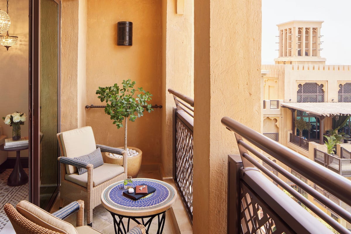 A balcony with wicker furniture, a potted plant, and a view of traditional buildings.