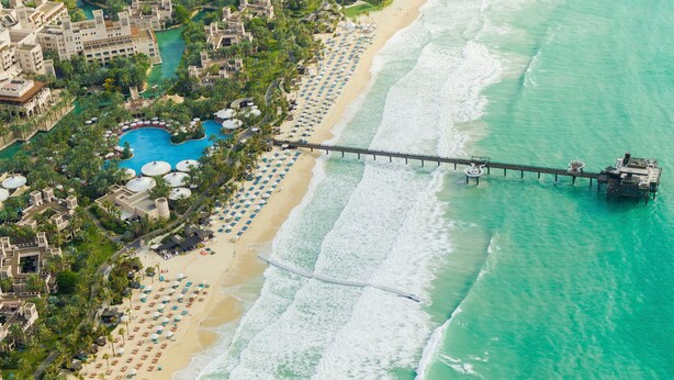 Vista aérea de un resort con playa, piscina y muelle que se adentra en el océano.