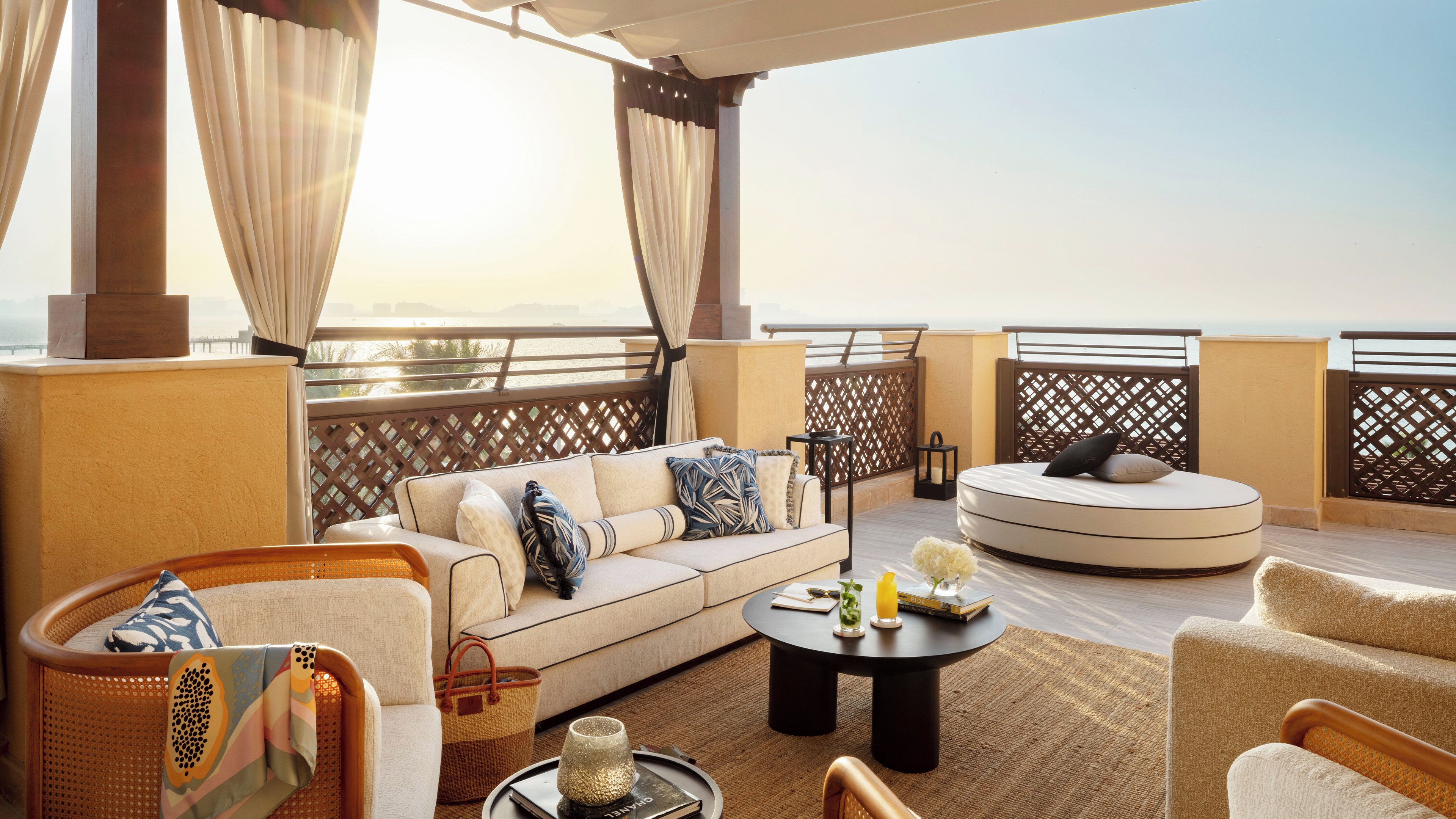 Een zonnig buitengebied met een bank, stoelen, een ronde tafel en uitzicht op zee.
