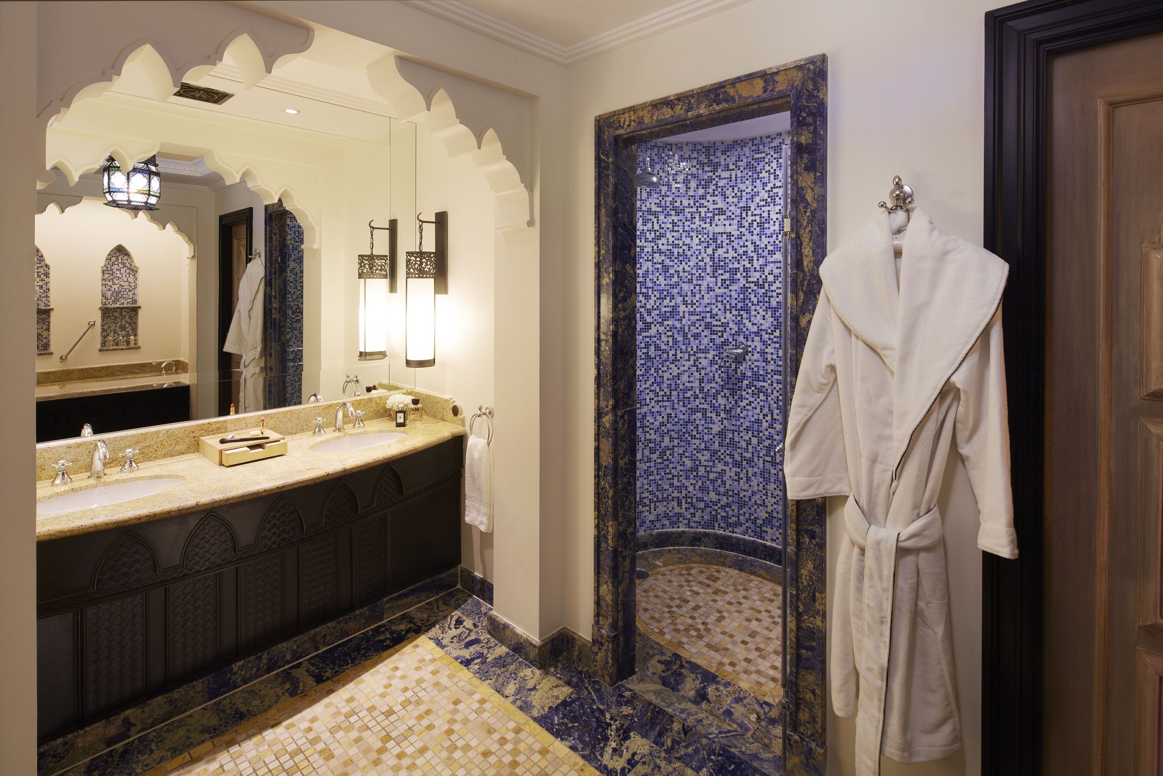 A bathroom with a double sink vanity, a large mirror, and a blue mosaic wall.