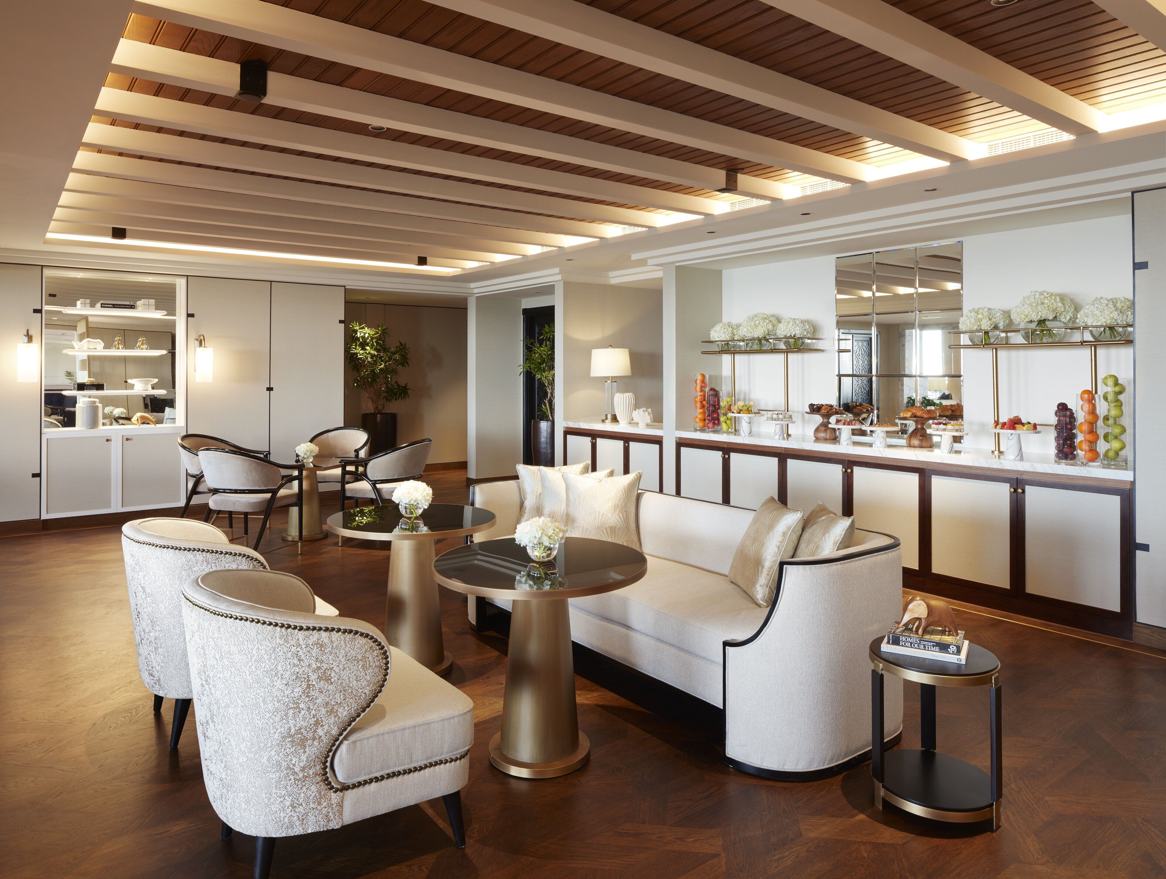 Un'ampia hall dalle linee moderne, con un'area salotto con divano e poltrone, un tavolino da caffè e una reception con esposizione di frutta e fiori.