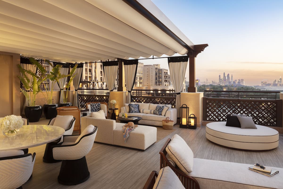 A modern outdoor seating area with a city skyline view, featuring a round seating area, a sofa, and a dining table with chairs.