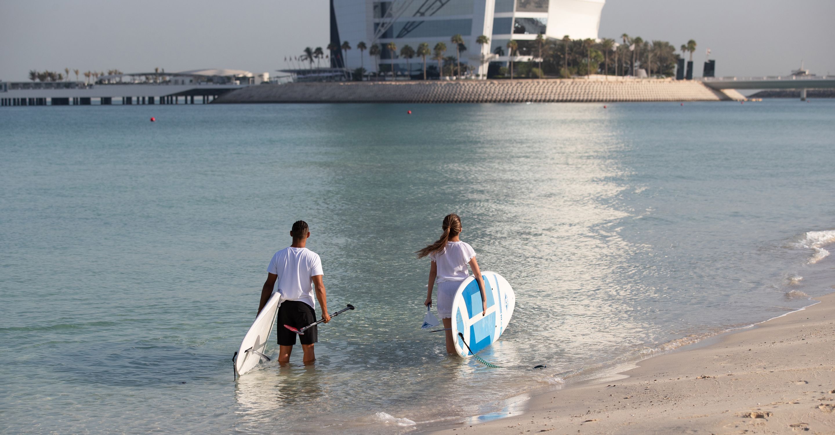 Dos personas caminando hacia la playa con tablas de surf.