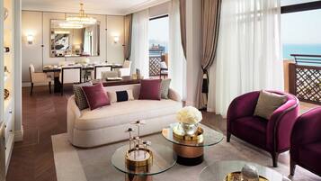 A modern hotel room with a sofa, armchairs, a dining area, and a balcony with a view of the sea.