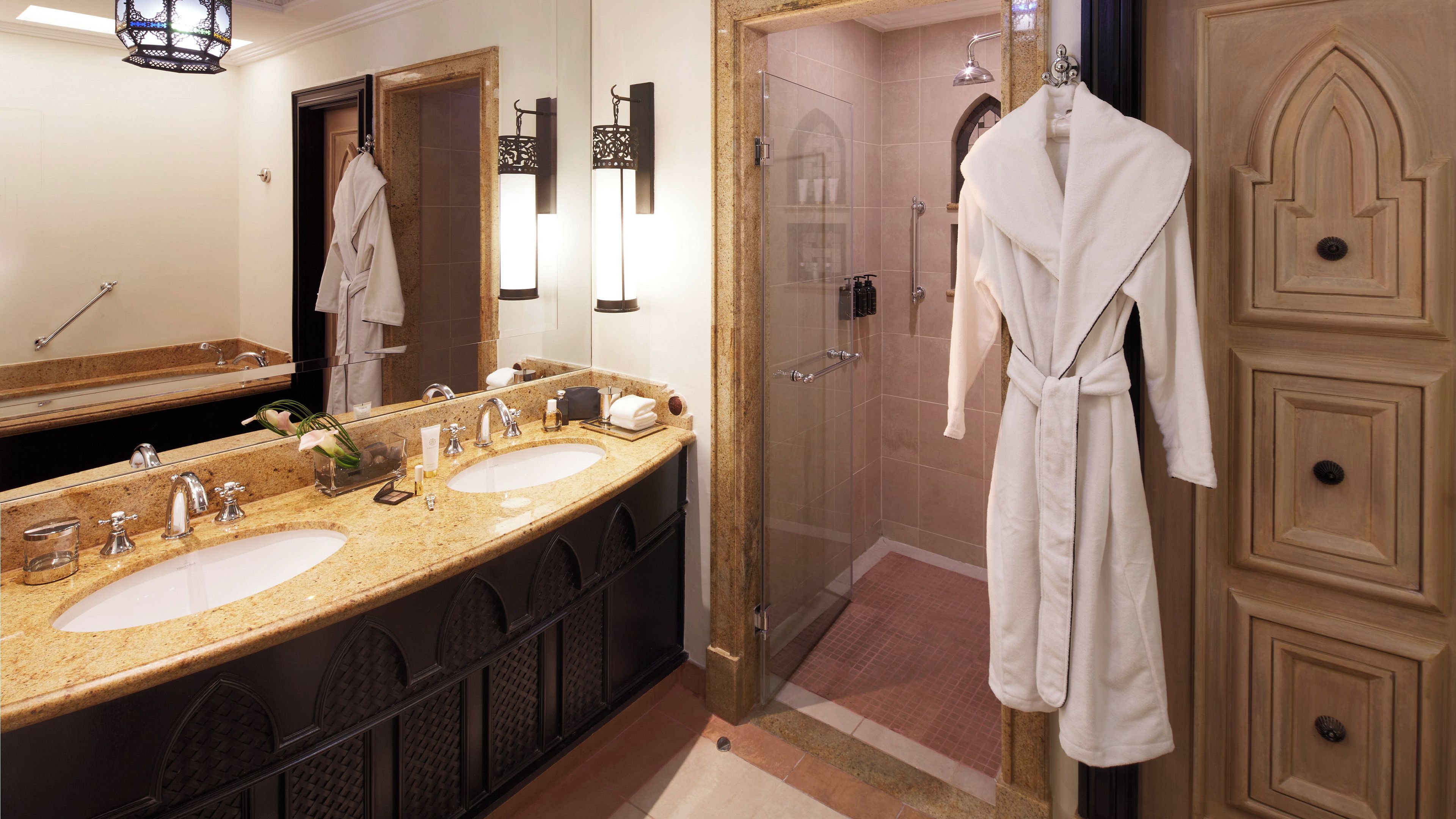 A hotel bathroom with two sinks, a glass shower enclosure, and a robe hanging on the wall.