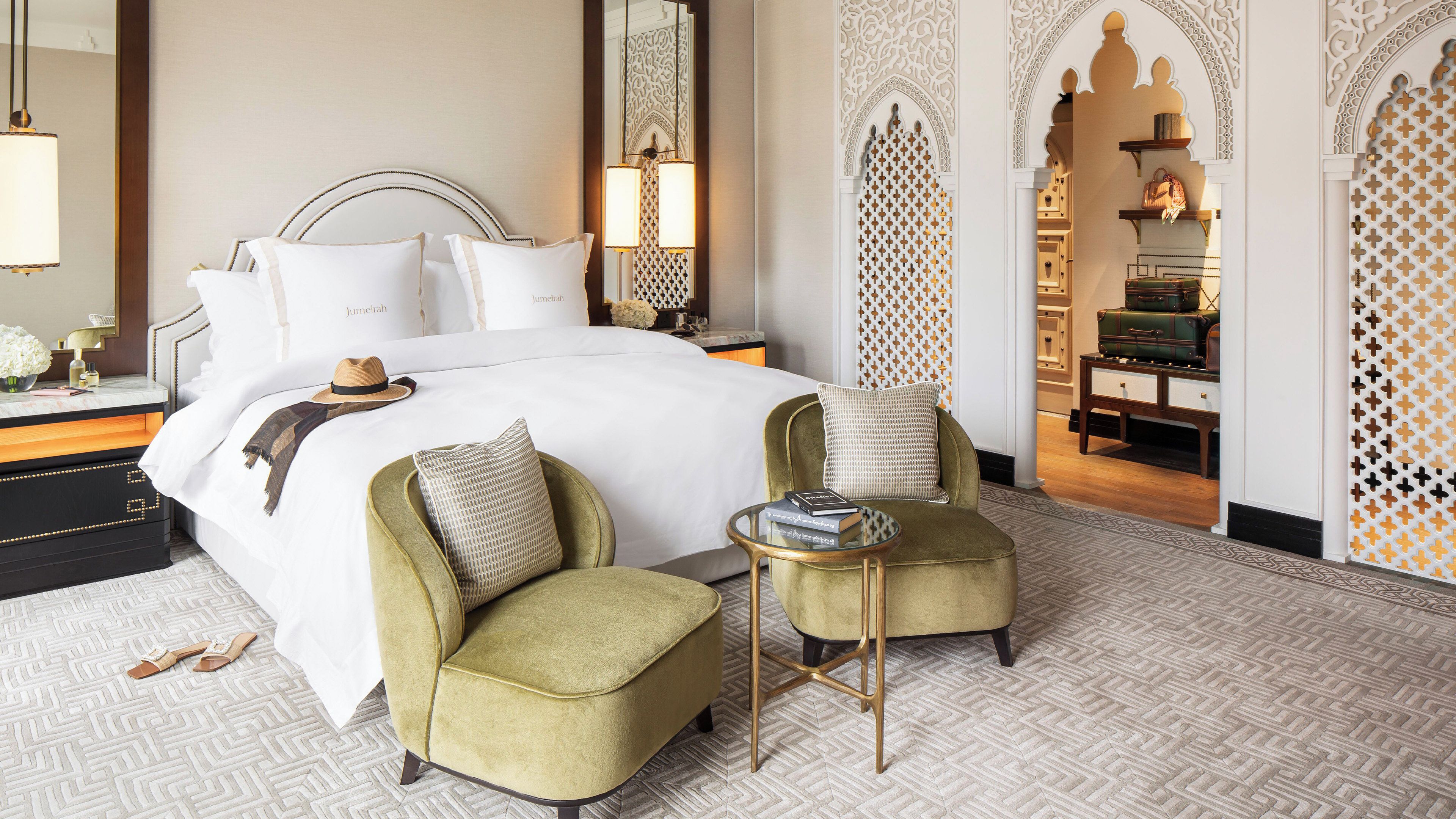 Habitación de hotel con una cama grande, dos sillones, una mesita y un espejo decorativo.