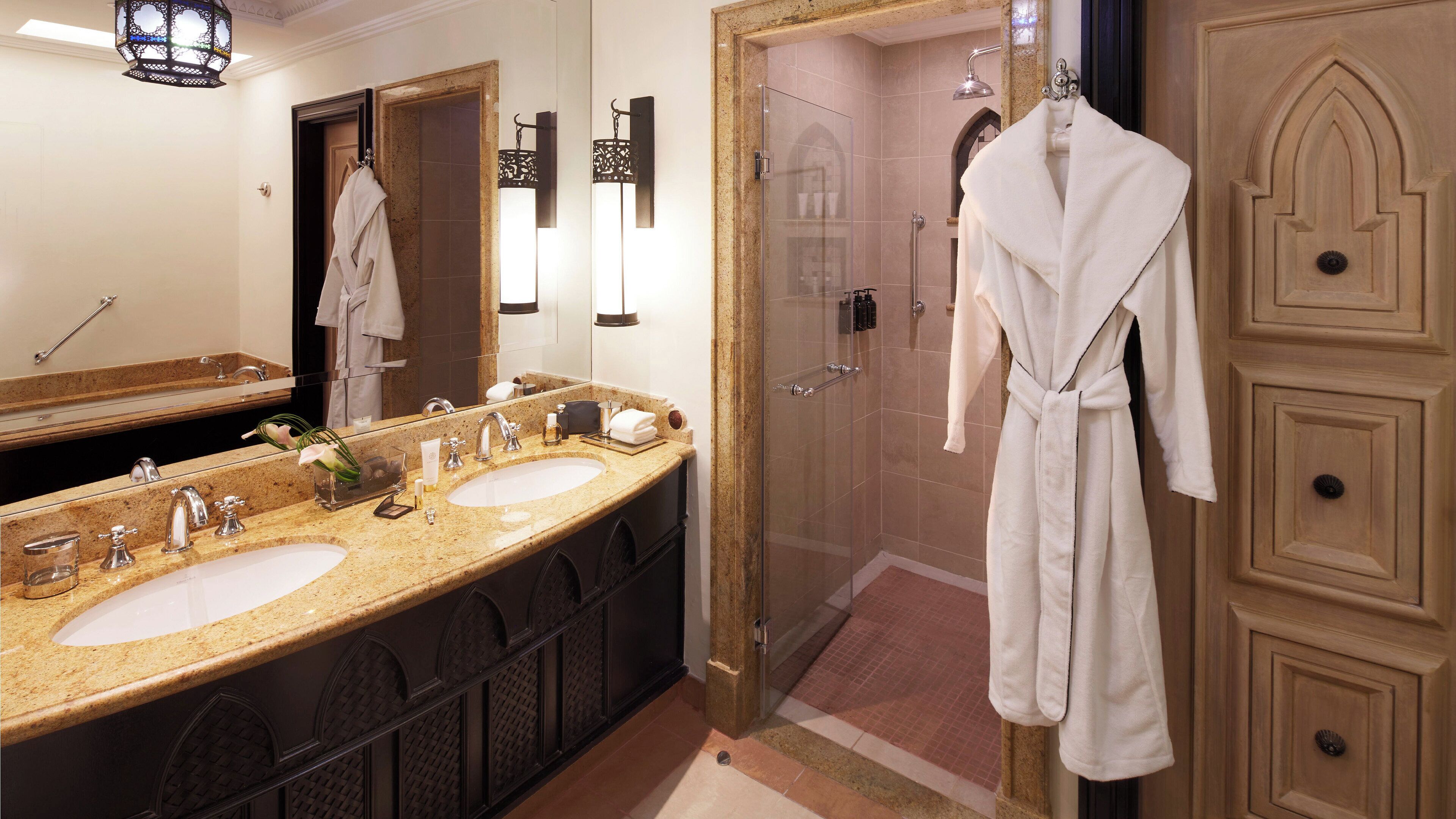 A bathroom with two sinks, a glass shower enclosure, and a robe hanging on a door.
