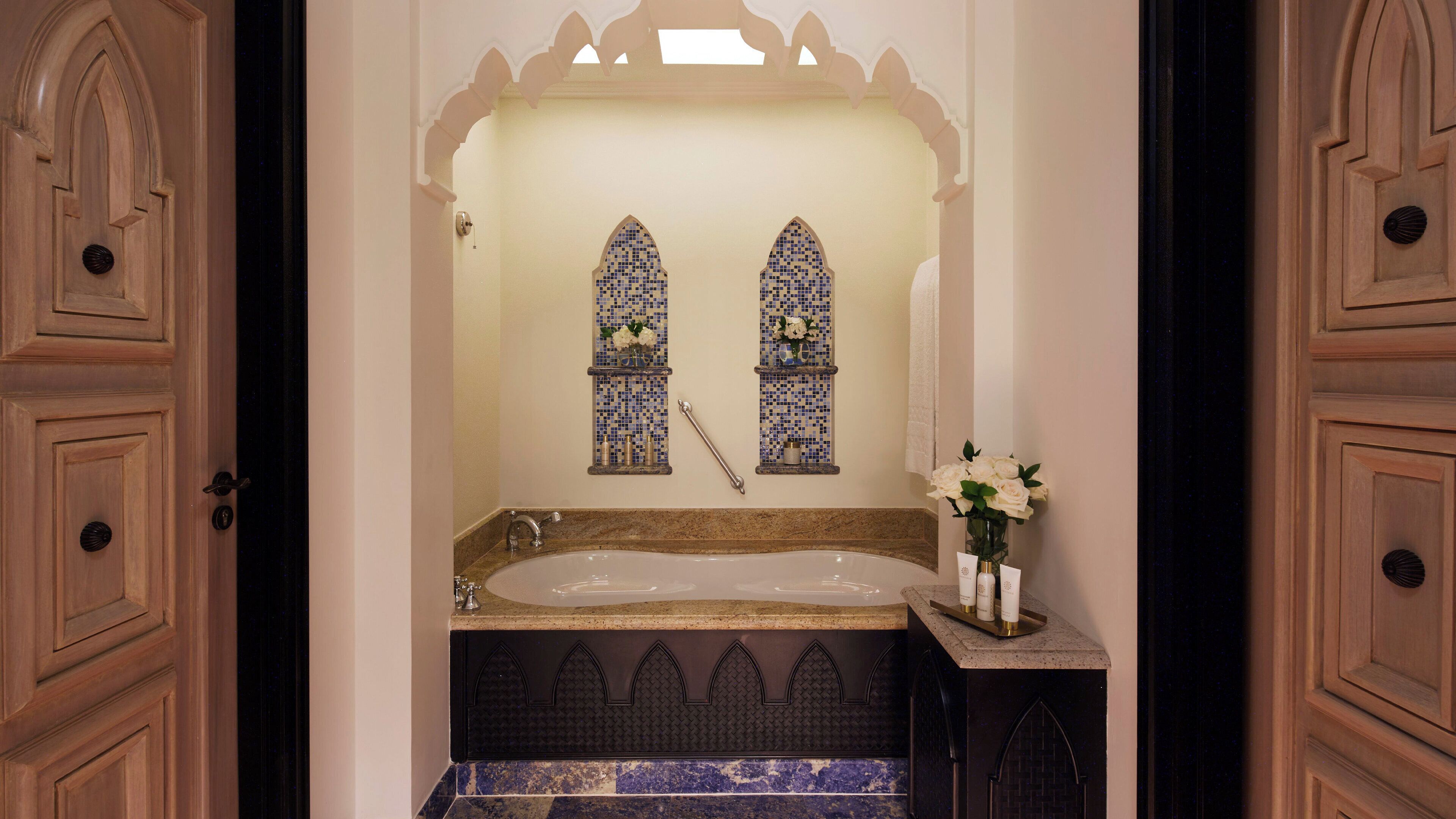 A bathroom with a freestanding bathtub, two wall-mounted sinks, and decorative tiles.