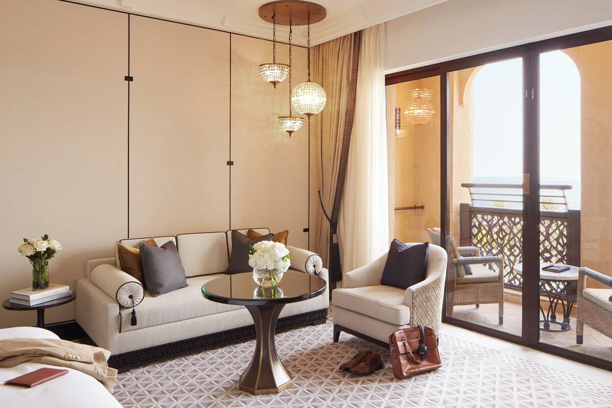 A hotel room with a sofa, armchair, round table, and a view of the balcony.