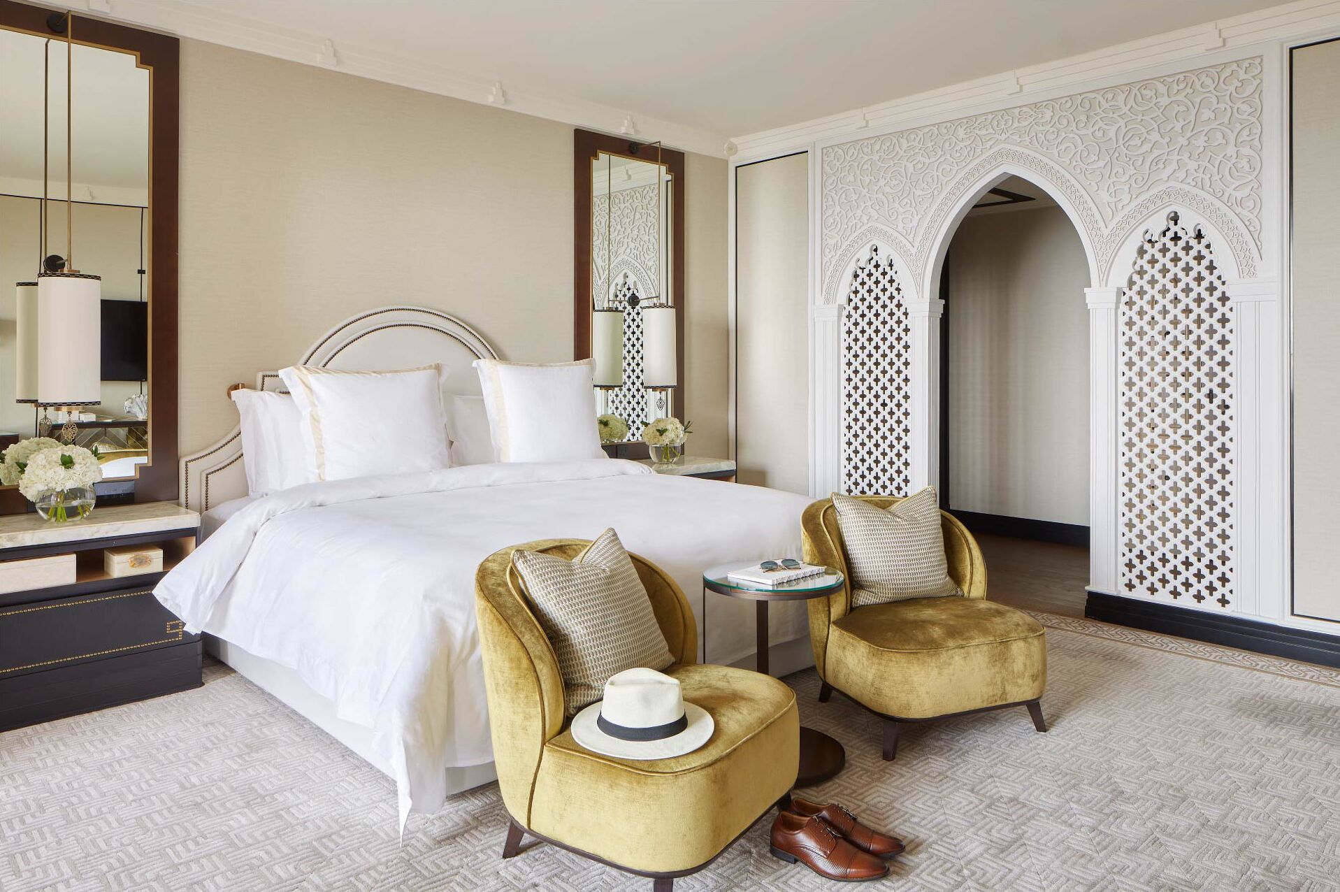 A hotel room with a large bed, two armchairs, a small table, and a mirror.