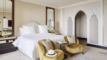 A hotel room with a large bed, two armchairs, a small table, and a mirror.