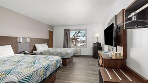 A hotel room with two beds, a TV, a desk with a lamp, and a window with curtains.