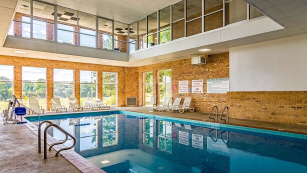 An indoor swimming pool with a view of the outdoors through large windows, a brick wall, and a ceiling with a grid pattern.