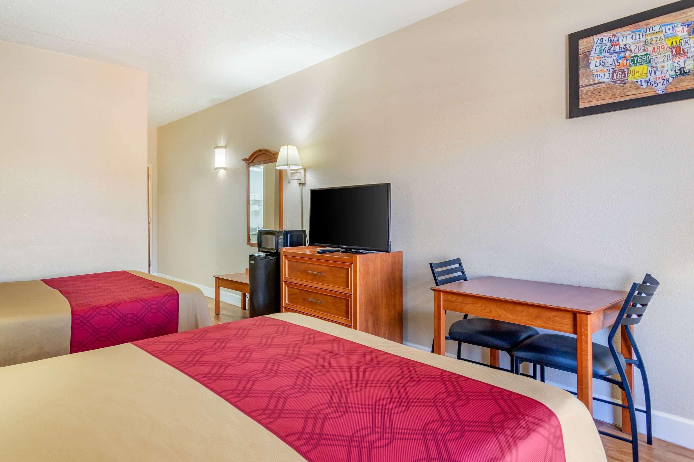 Habitación de hotel con dos camas, un escritorio, una silla, un televisor y una obra de arte colgada en la pared.