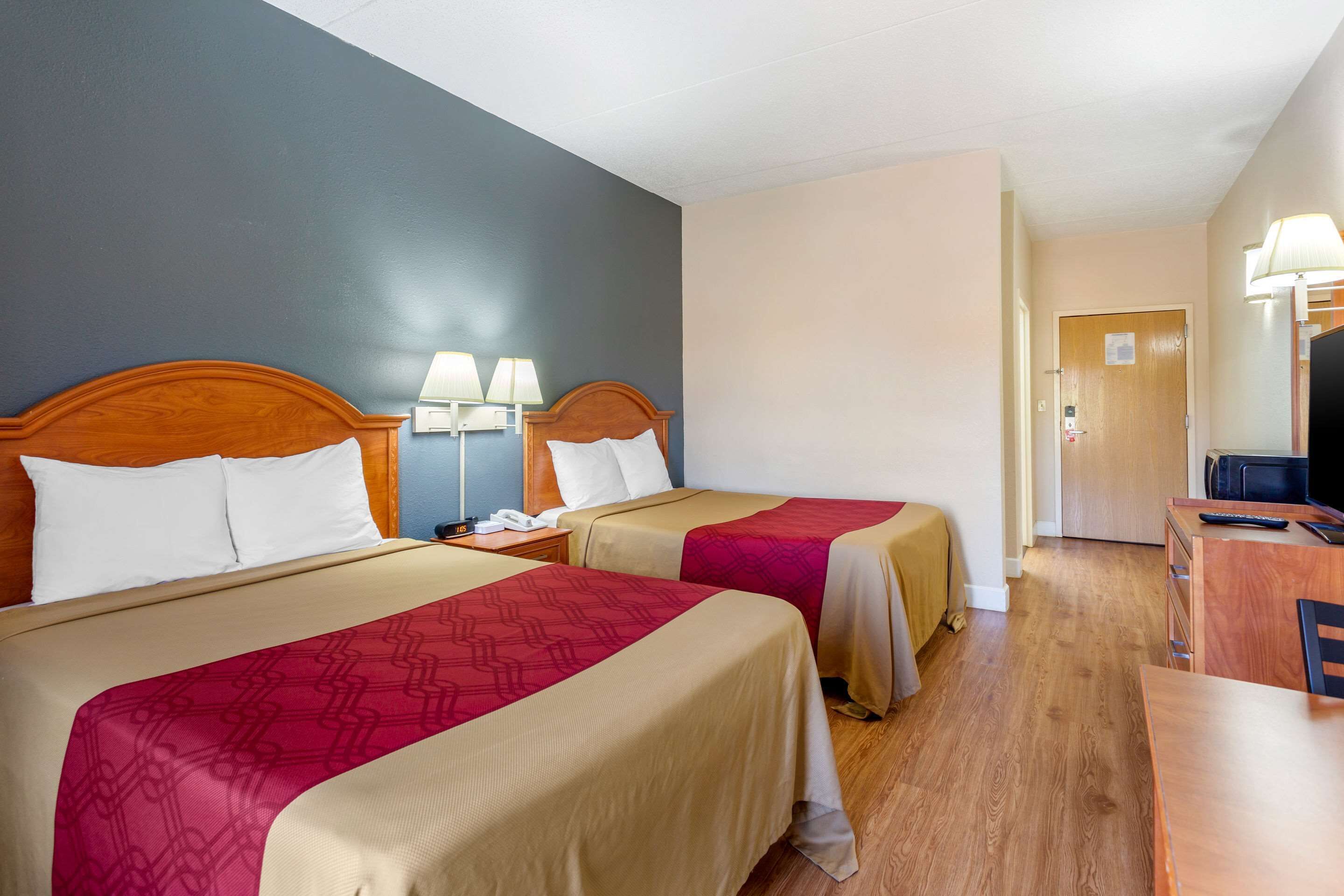 A hotel room with two beds, a desk, a TV, and a lamp.