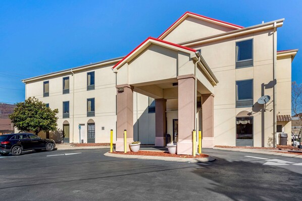 A multi-story hotel with a covered entrance, a parking lot, and a tree in front.