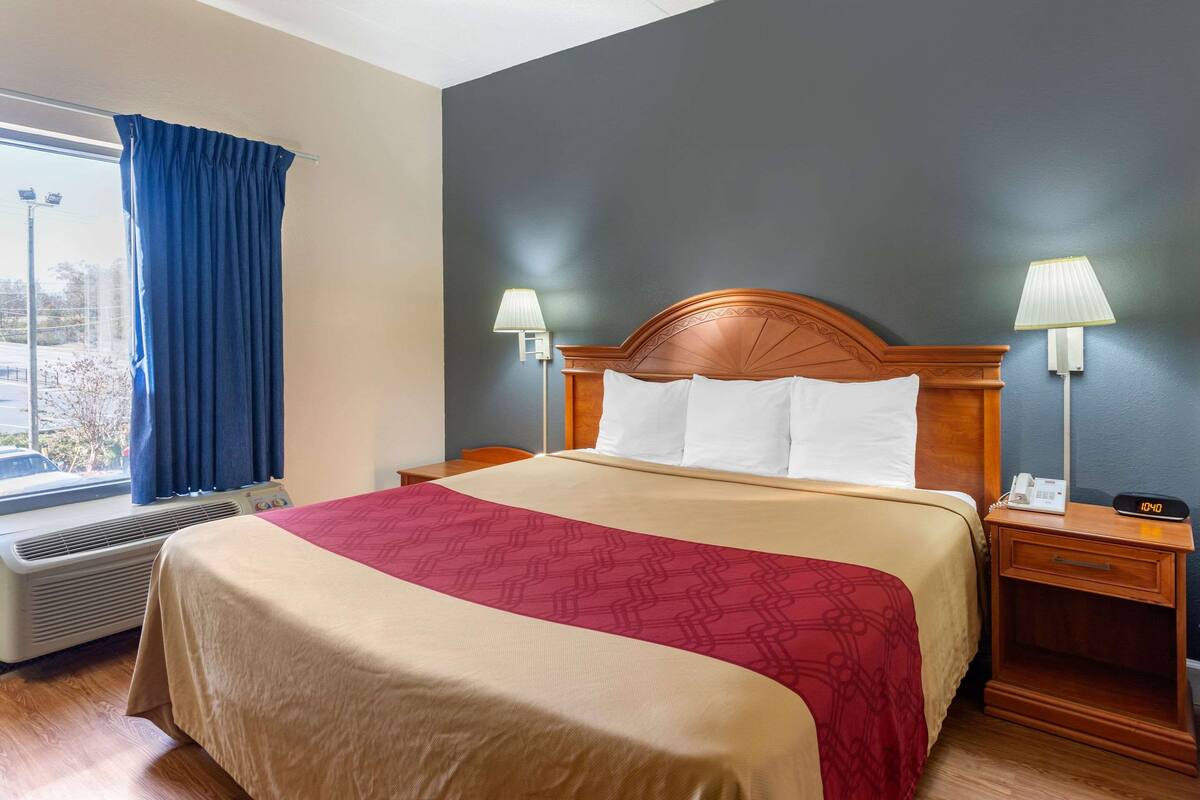 A hotel room with a large bed, two bedside lamps, a nightstand with a phone, and a window with curtains.