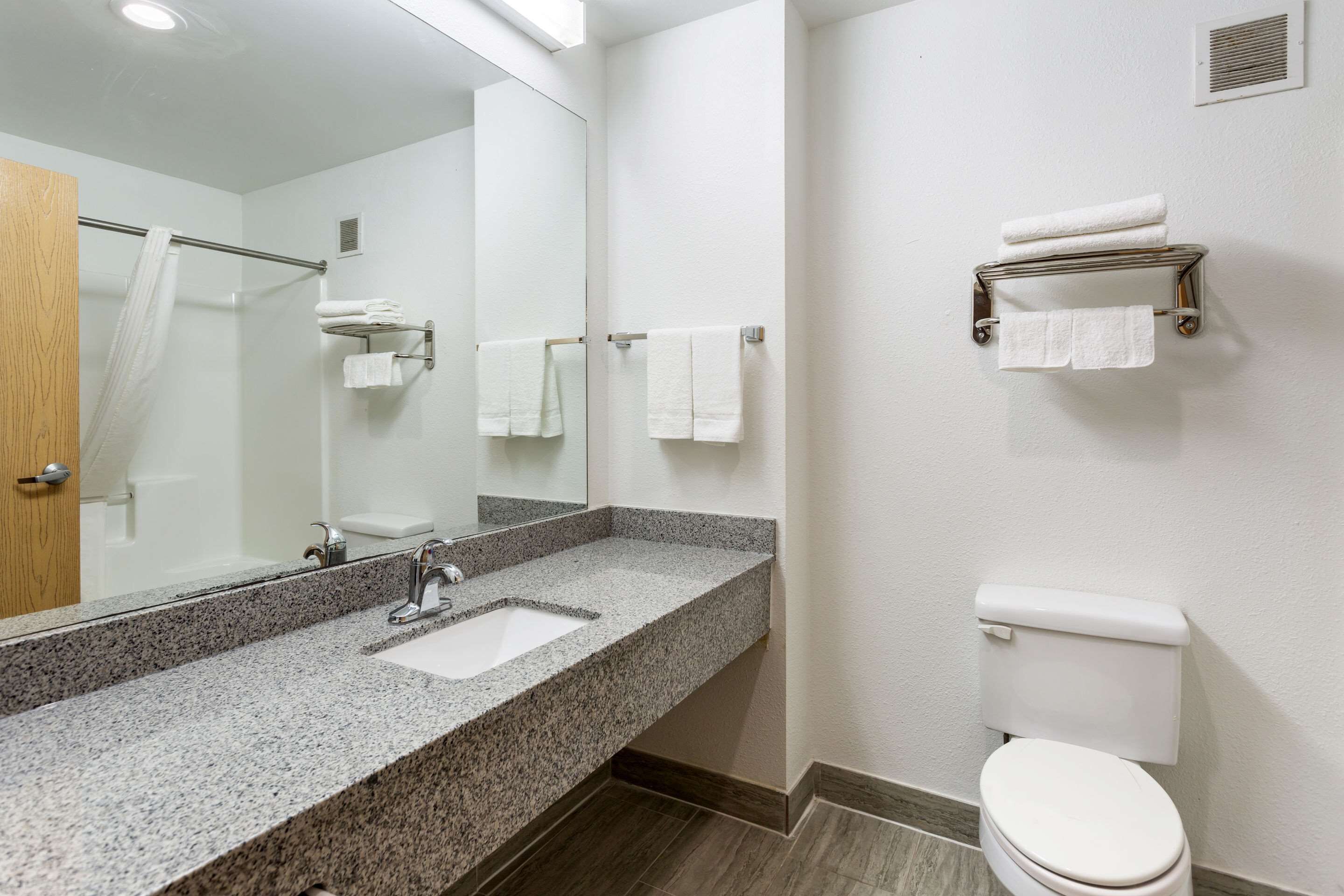 Un baño con lavamanos de granito, espejo, inodoro y toalleros.