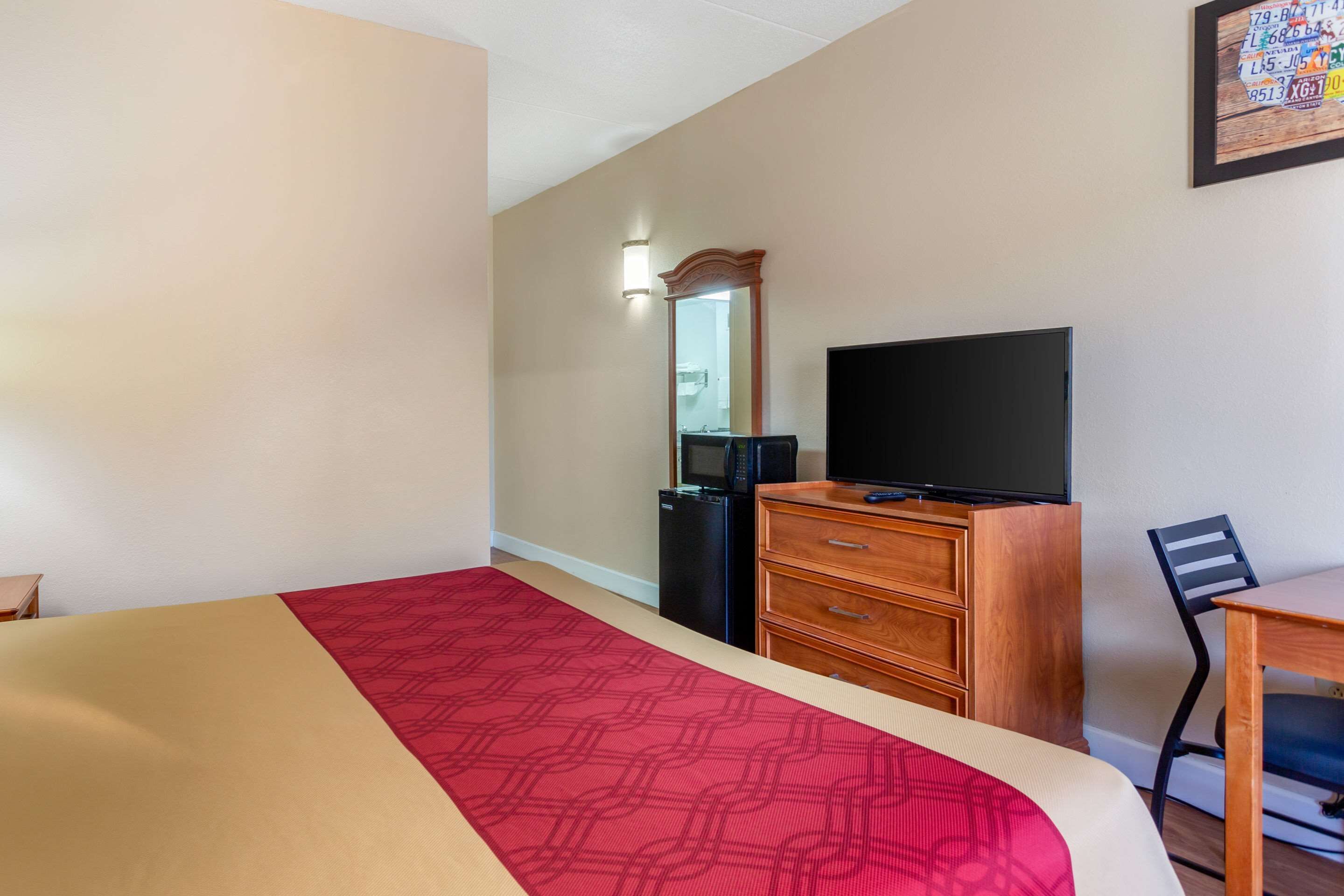 Ein Hotelzimmer mit Bett, Fernseher, Kommode, Schreibtisch und Stuhl.