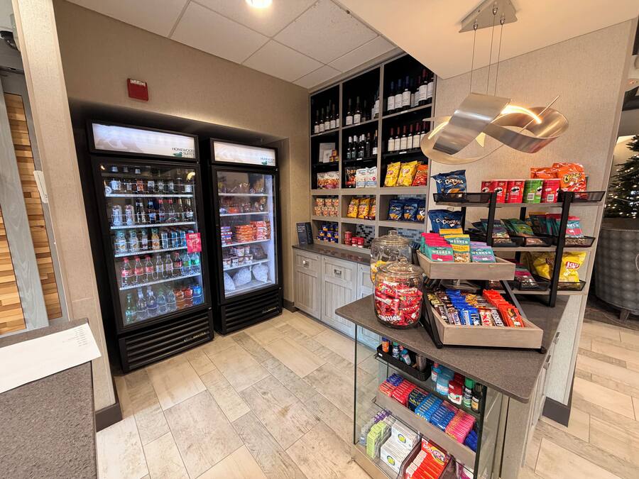 A hotel lobby with a self-service beverage station, snack dispensers, and a display of bottled water and snacks.
