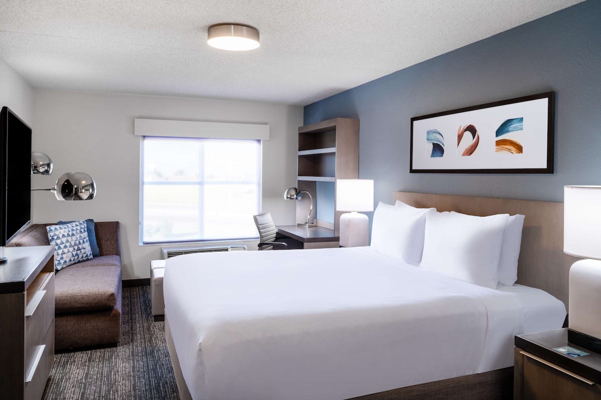 A hotel room with a large bed, a desk, a chair, a TV, and a window.