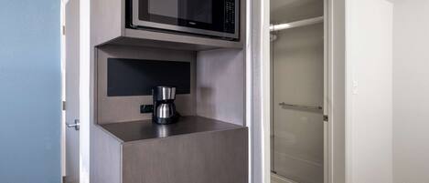 A compact kitchenette with a microwave and coffee maker, a sliding door closet, and a shower area.
