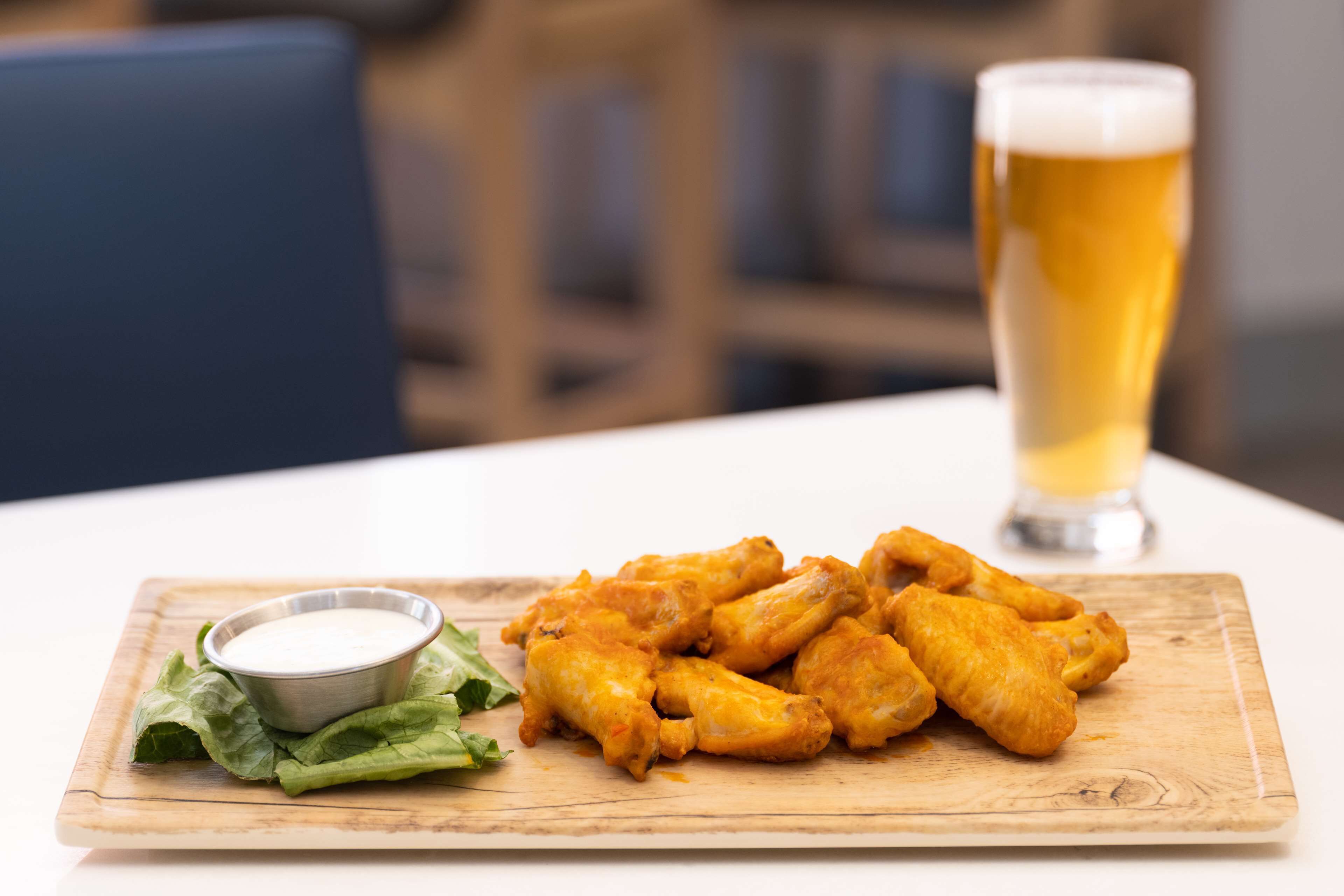 Un plato de alitas de pollo con salsa para mojar y una jarra de cerveza sobre una mesa de madera.