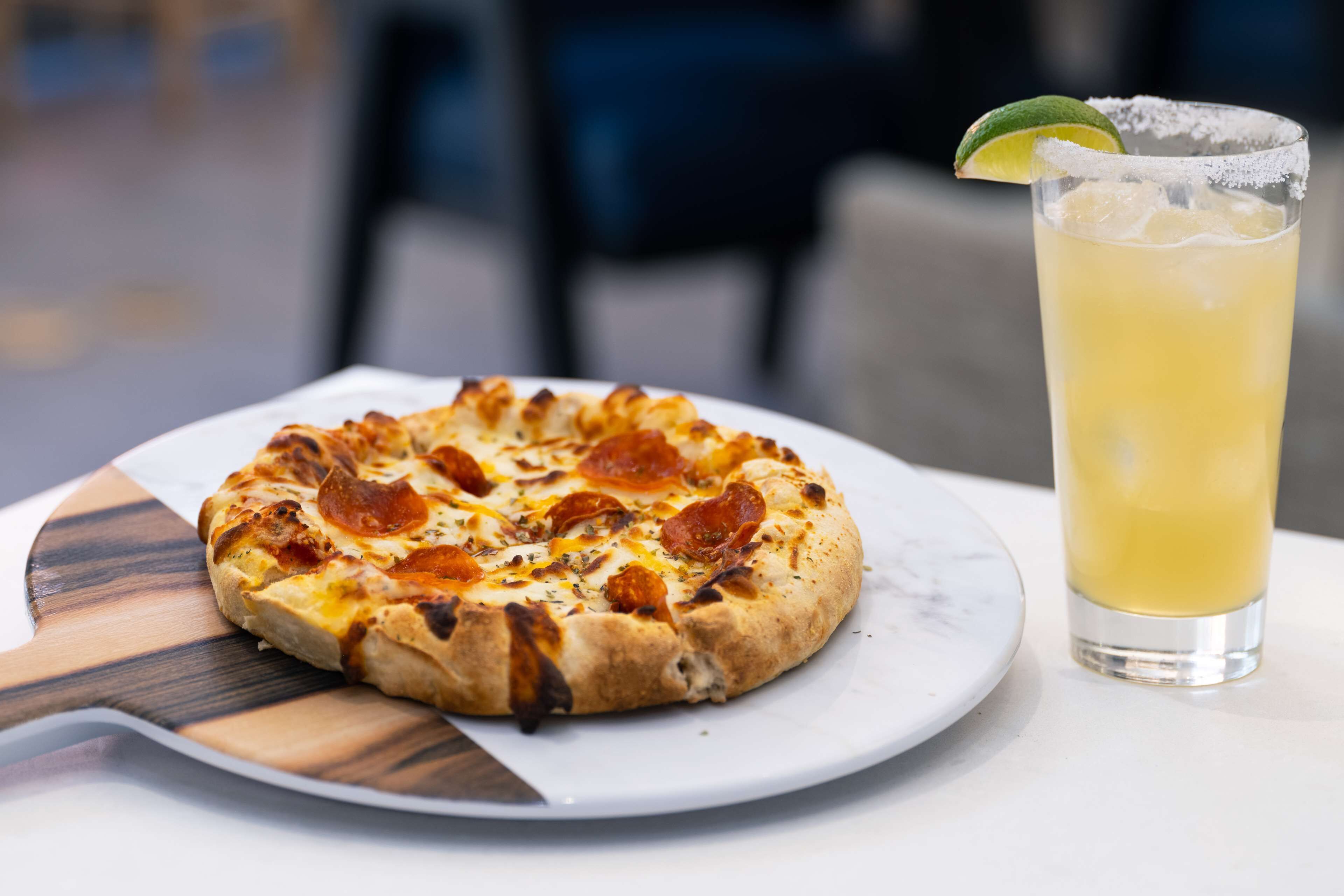 Une pizza à la saucisse piquante, accompagn ée d’un verre de boisson fraîche et d’une tranche de citron vert, le tout servi sur une assiette blanche.