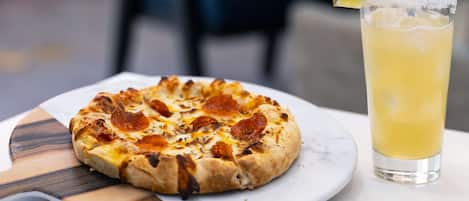 A pizza with pepperoni and a glass of iced beverage with a lime wedge on a white plate.