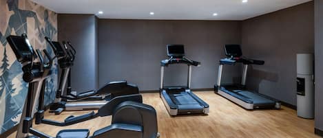 Uma academia com várias esteiras, elípticos e uma bicicleta ergométrica.