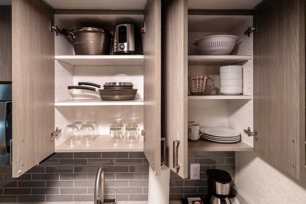 A kitchen with open cabinets displaying cookware, glassware, and dishes.