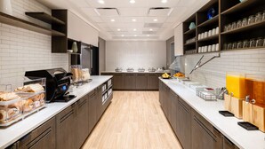 Cocina moderna con salpicadero de azulejos blancos, armarios de madera e isla central con cafetera y exposición de fruta.
