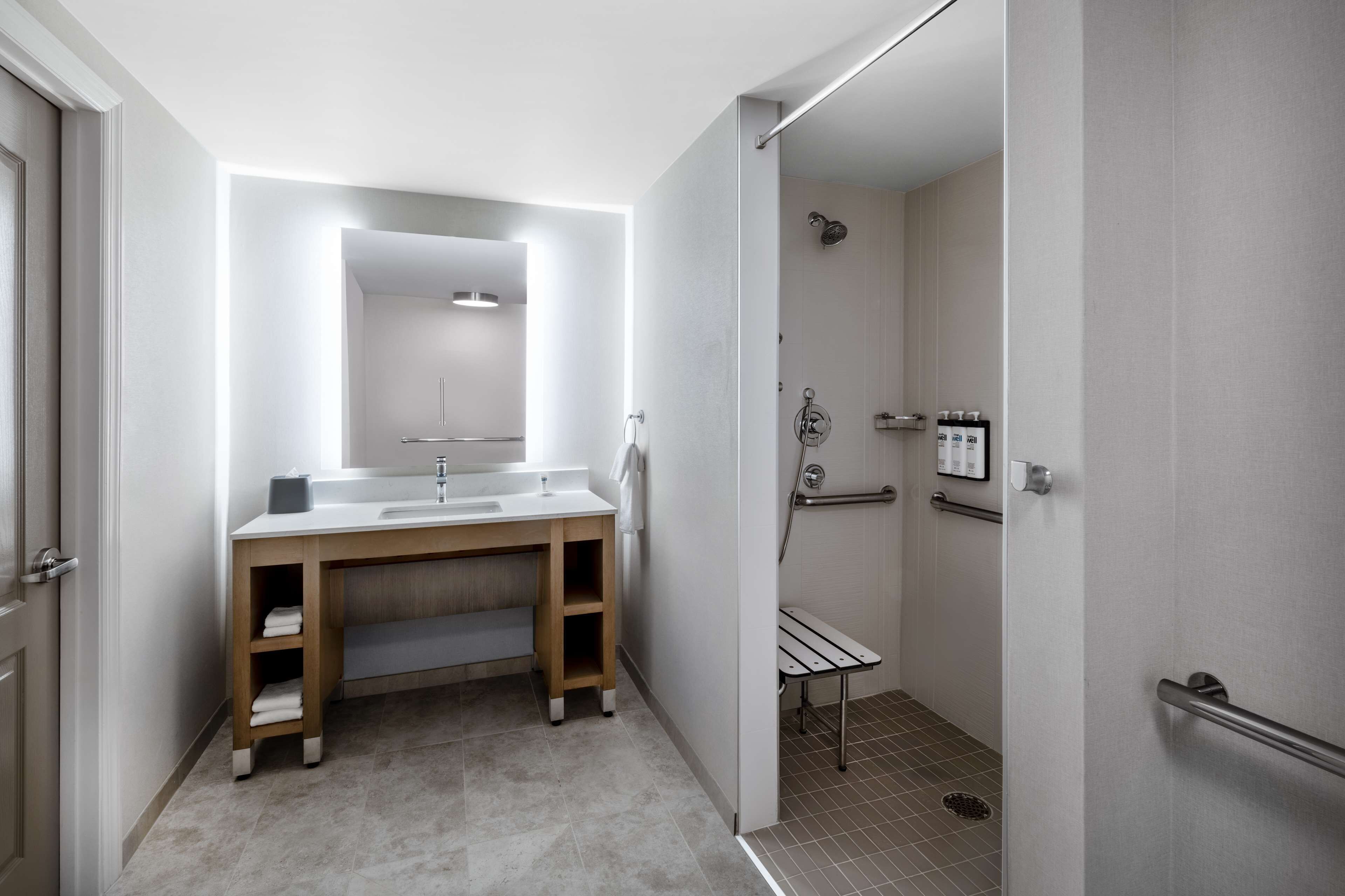 Ein modernes Badezimmer mit einem Holzbadezimmermöbel, einem großen Spiegel, einer Dusche mit Glastür und einer Haltestange.