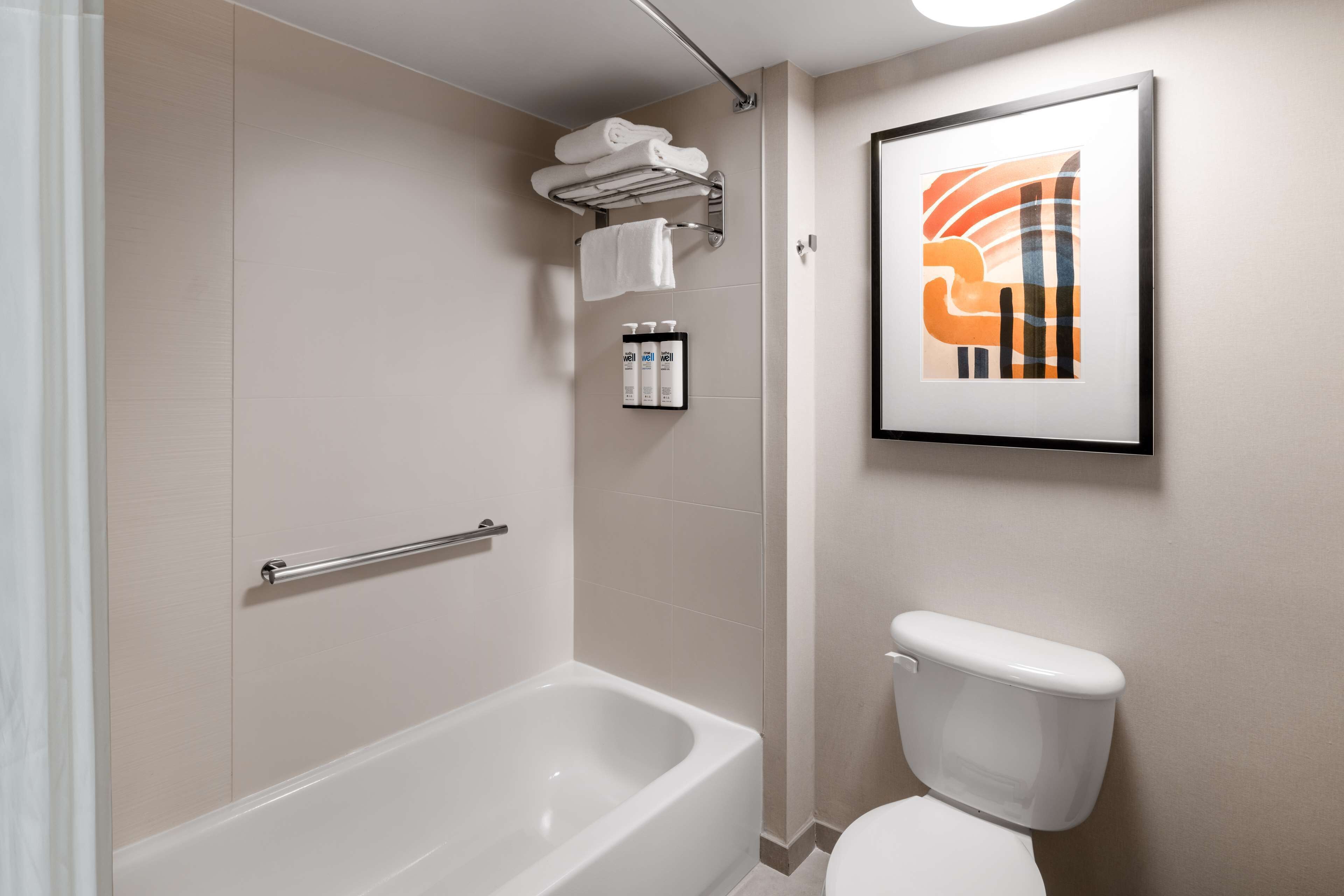 A modern bathroom with a bathtub, toilet, and a framed abstract artwork on the wall.
