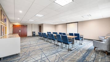 Un salón de conferencias con una larga mesa, sillas azules, una pantalla de proyector y suelo alfombrado.