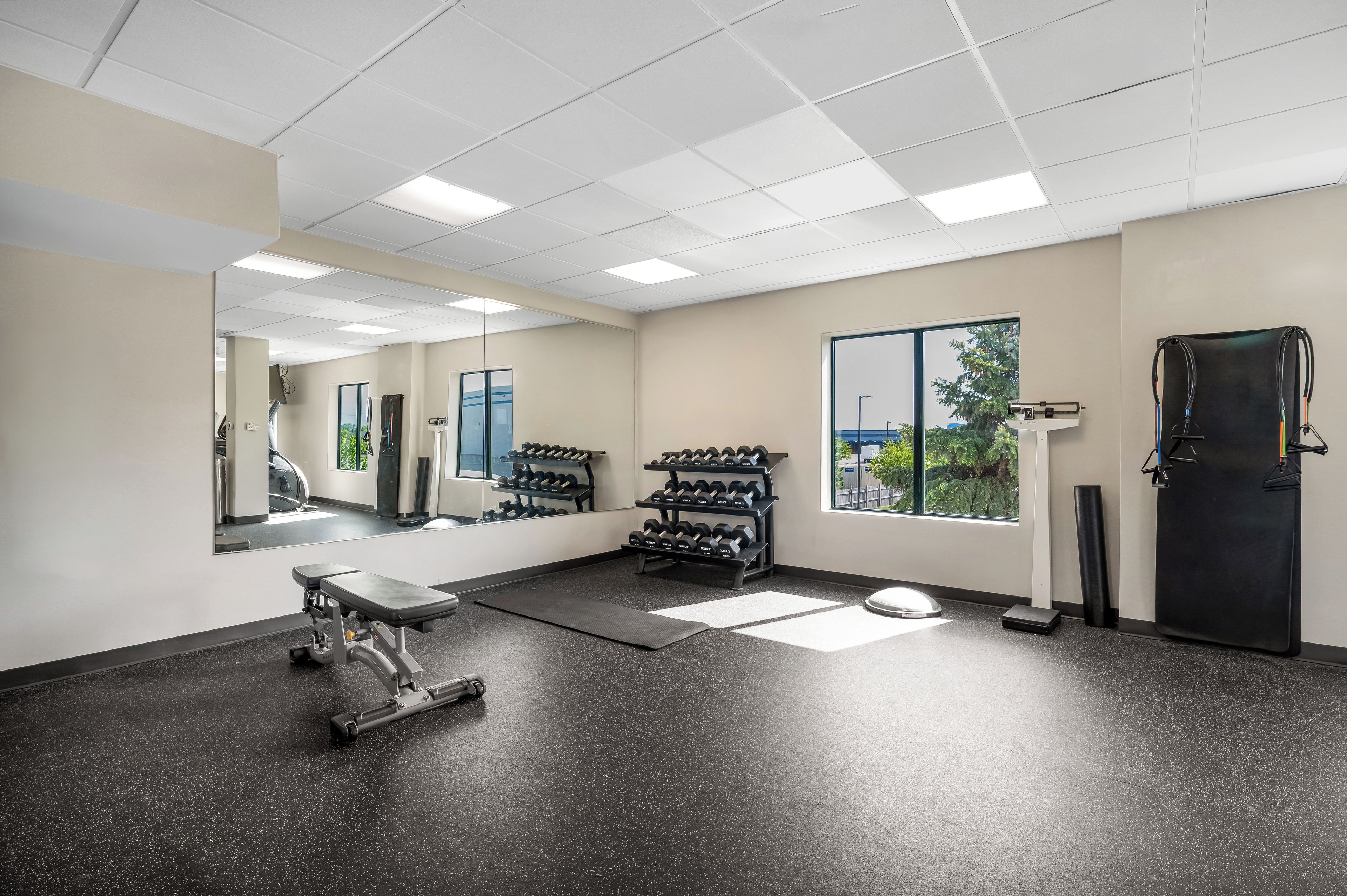 Ein Fitnessraum mit Trainingsgeräten, einer Spiegelwand und einem Fenster mit Blick.