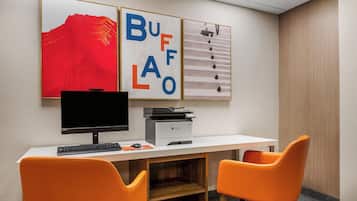 Un espacio de trabajo con un escritorio, dos sillas naranjas, un monitor de computadora, una impresora y tres cuadros en la pared.