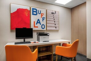 Un espacio de trabajo con un escritorio, dos sillas naranjas, un monitor de computadora, una impresora y tres cuadros en la pared.