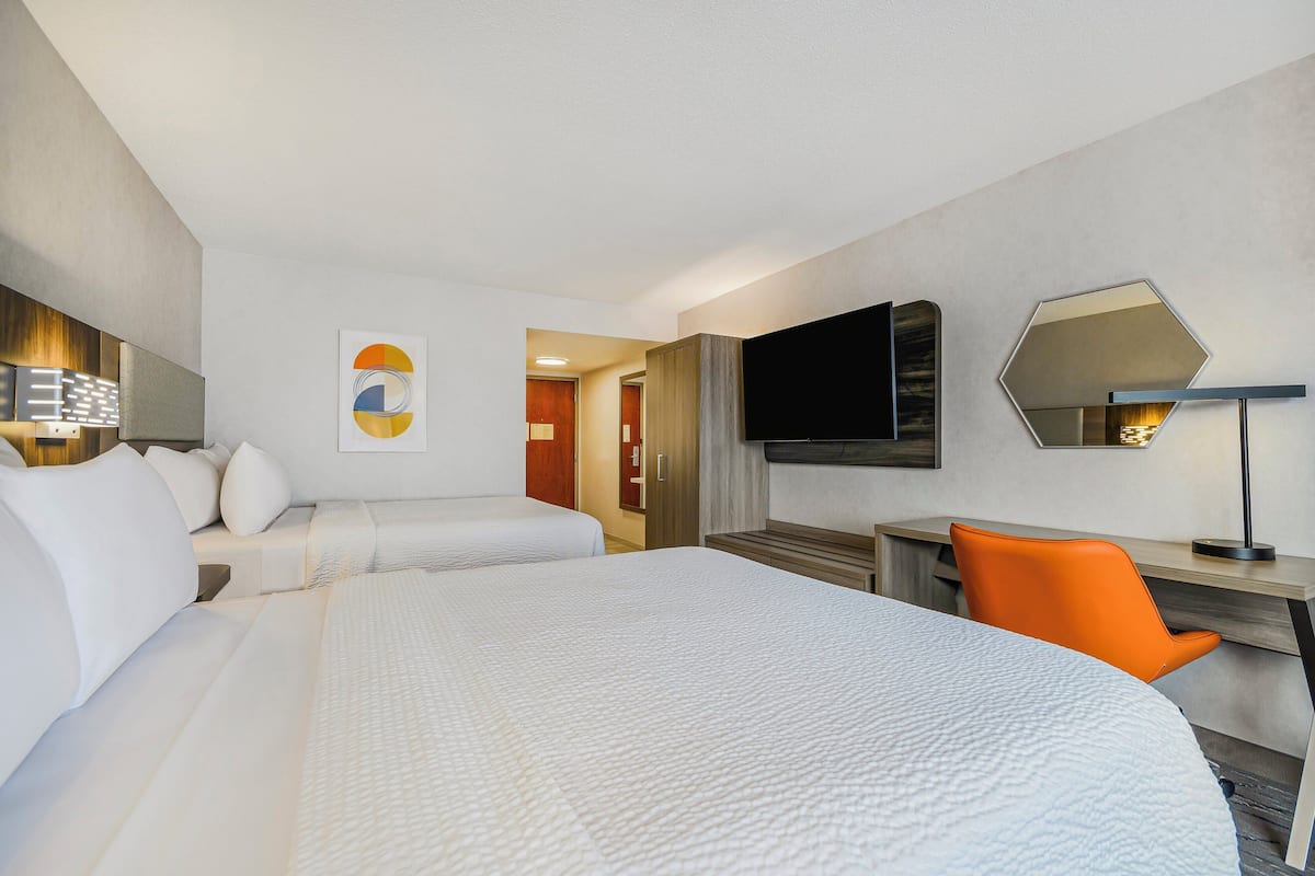 Ett hotellrum med två sängar, ett skrivbord, en orange stol, en platt-TV och en stor spegel.