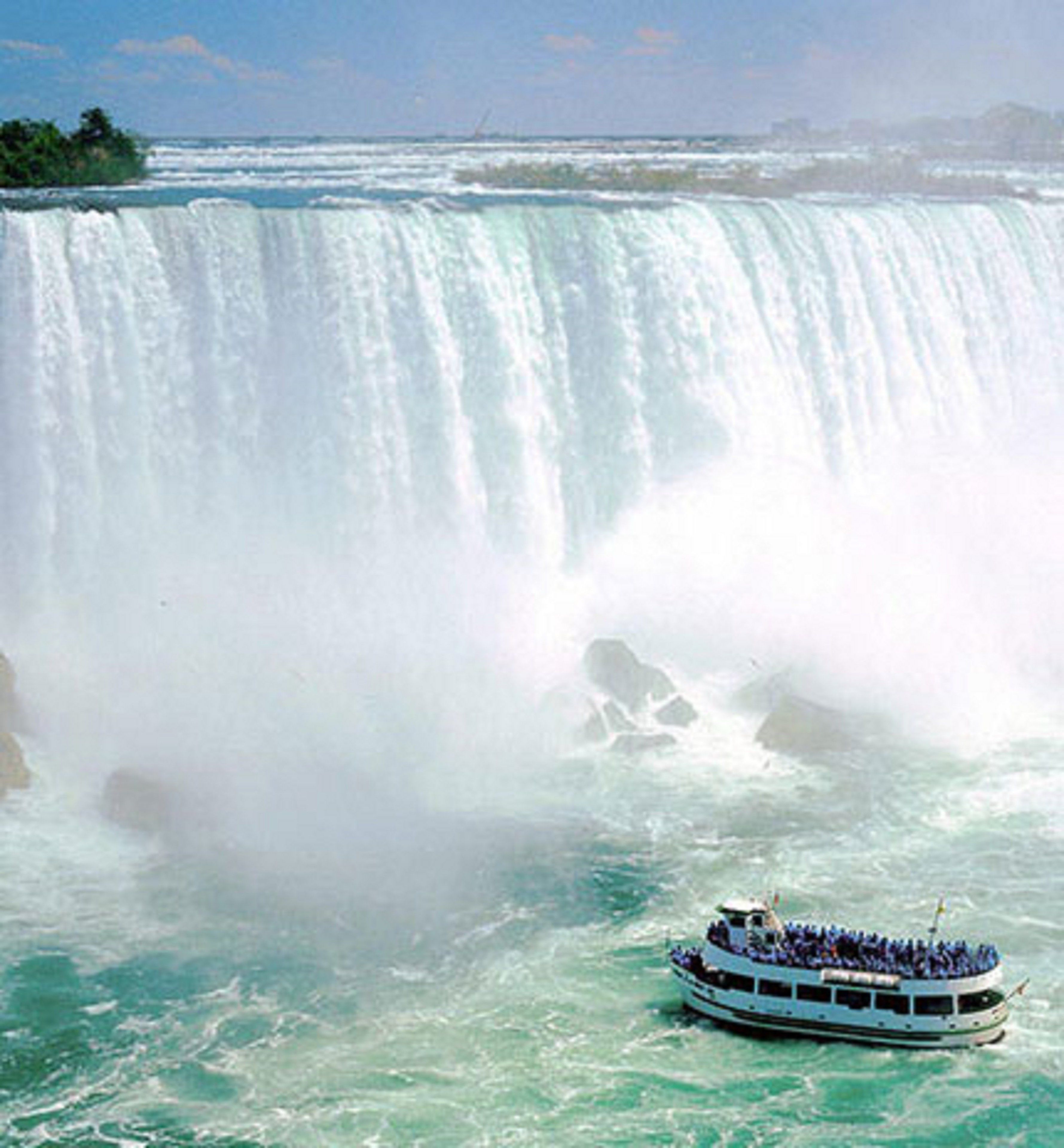 A boat with passengers in front of a large waterfall.