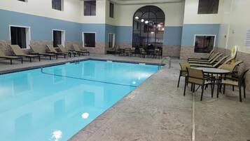 Una piscina con sillones y mesas, rodeada de muros de piedra y ventanas.