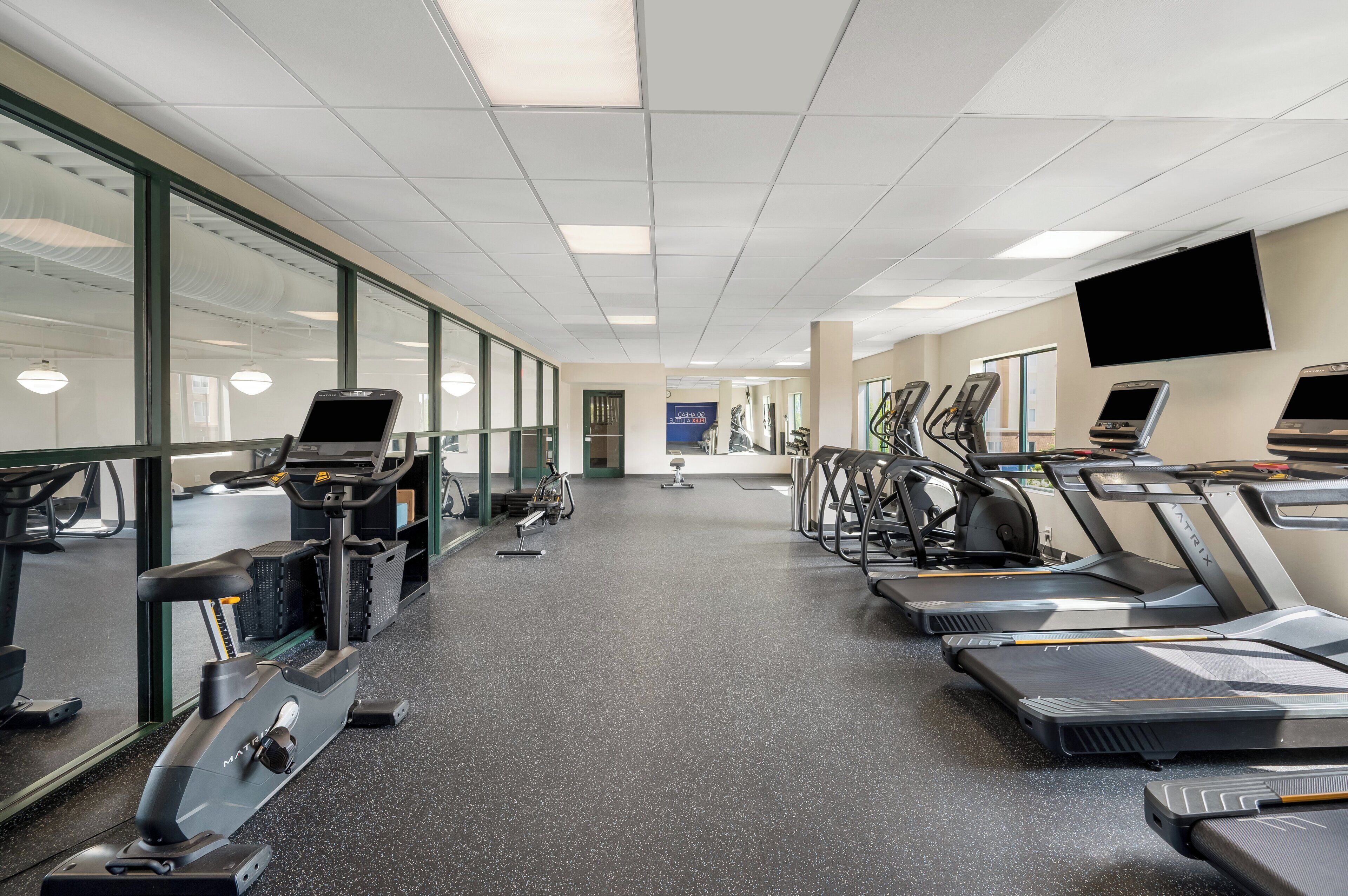 A gym with treadmills, exercise bikes, and a mirrored wall.