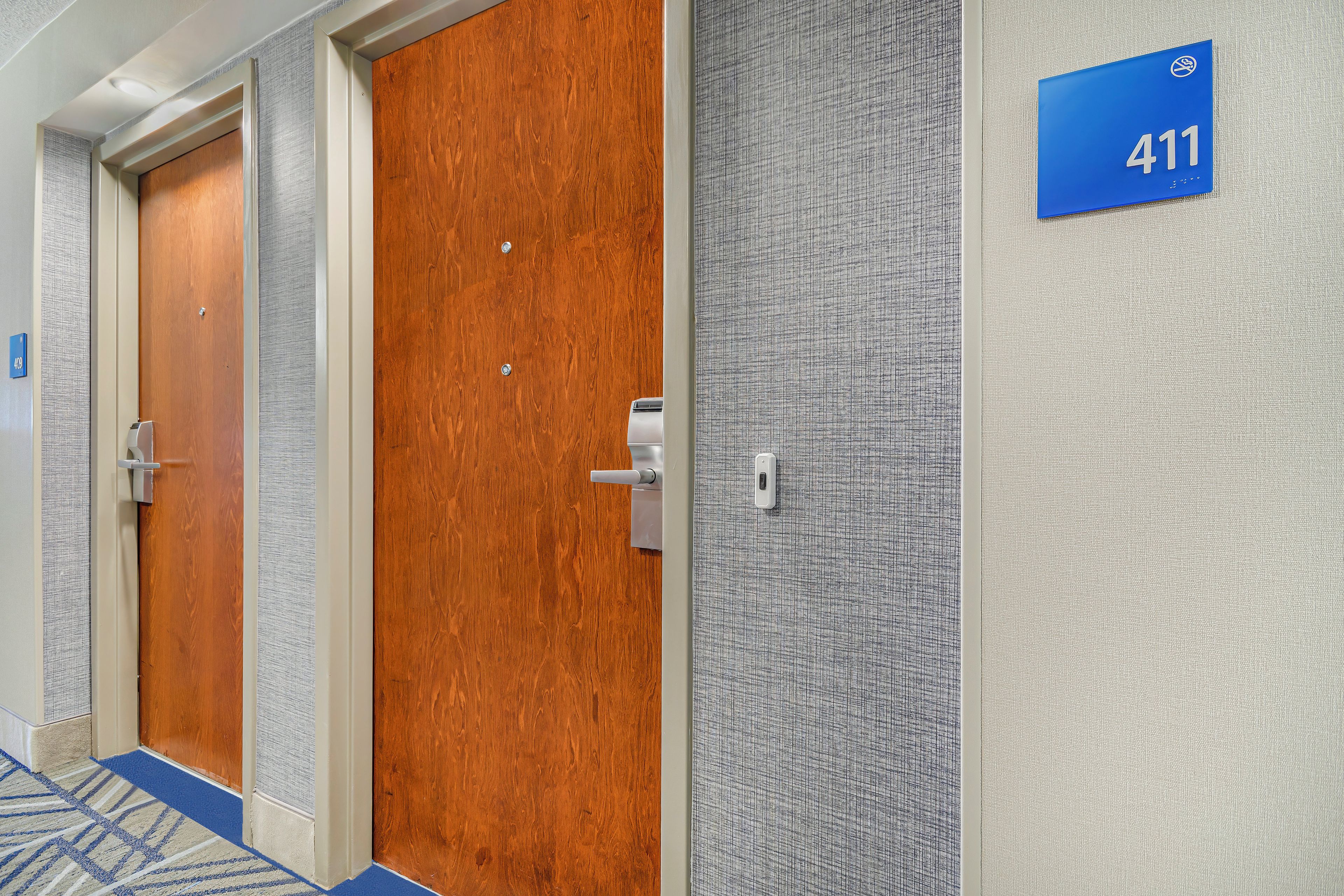 A hotel corridor with three doors, a blue sign with the number 411, and a textured wall.