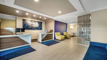 A hotel reception area with a reception desk, a computer, a seating area with chairs, and a decorative wall.