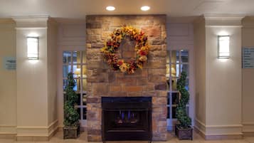 A stone fireplace with a decorative wreath, flanked by two potted plants.